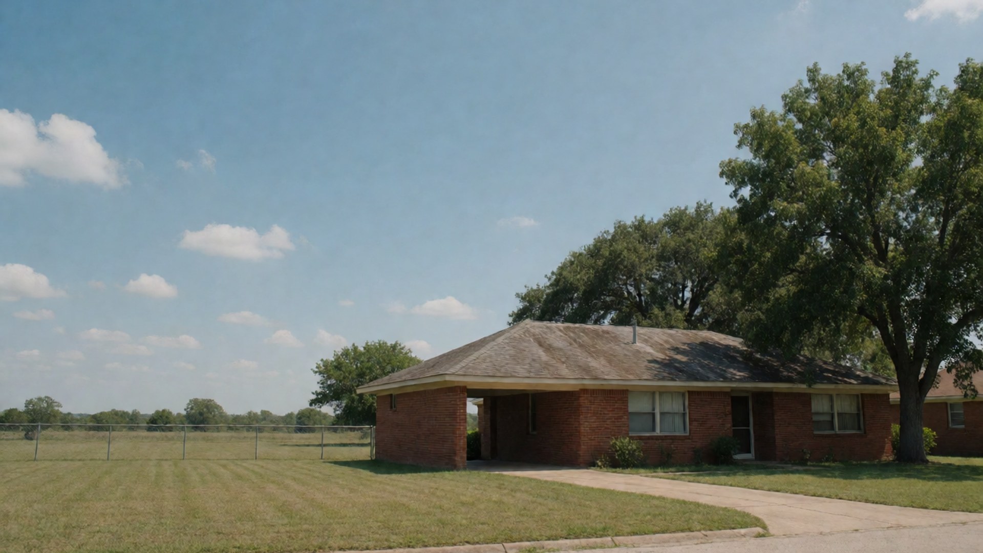 One-story brick ranch home beside a large oak tree on an open lot