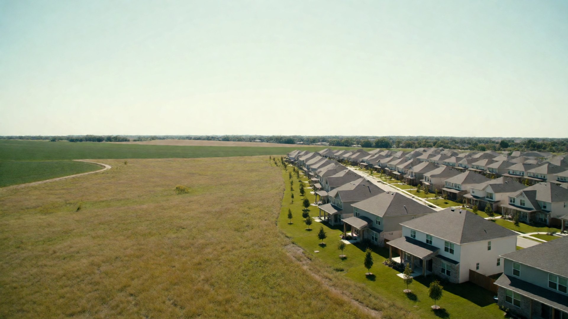 New subdivision rooftops at the edge of open prairie, seen from above